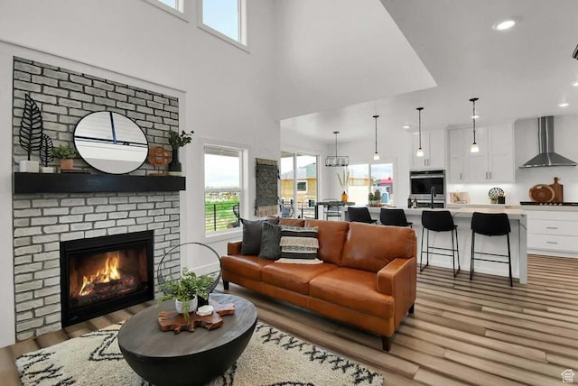 living room featuring light wood-style floors, healthy amount of natural light, recessed lighting, a brick fireplace, and a towering ceiling