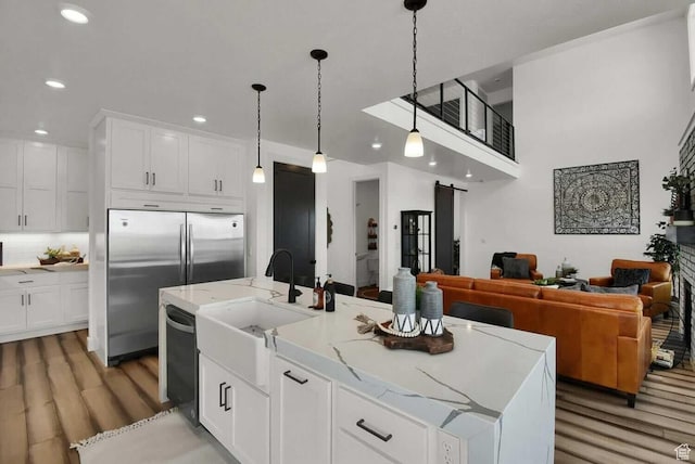kitchen featuring light wood finished floors, stainless steel refrigerator, a sink, white cabinetry, and recessed lighting