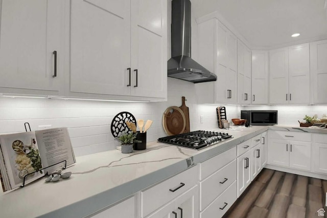 kitchen with wall chimney range hood, stainless steel appliances, white cabinets, tasteful backsplash, and recessed lighting