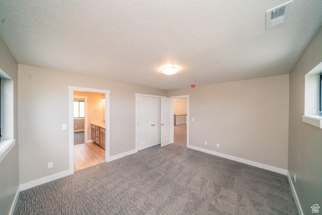 unfurnished bedroom with carpet floors, baseboards, a textured ceiling, ensuite bath, and a closet
