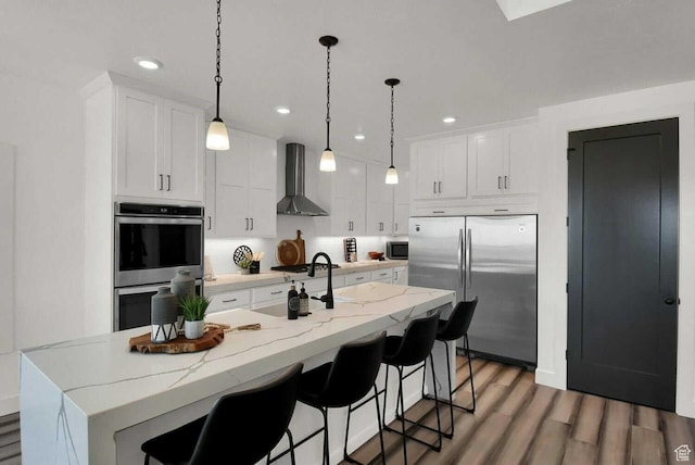 kitchen featuring wall chimney range hood, appliances with stainless steel finishes, recessed lighting, light wood-style flooring, and white cabinetry