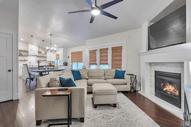 living room featuring a ceiling fan, a chandelier, dark wood finished floors, and a glass covered fireplace