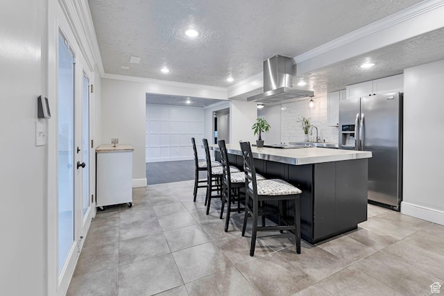 kitchen with stainless steel refrigerator with ice dispenser, island exhaust hood, crown molding, a textured ceiling, and a breakfast bar
