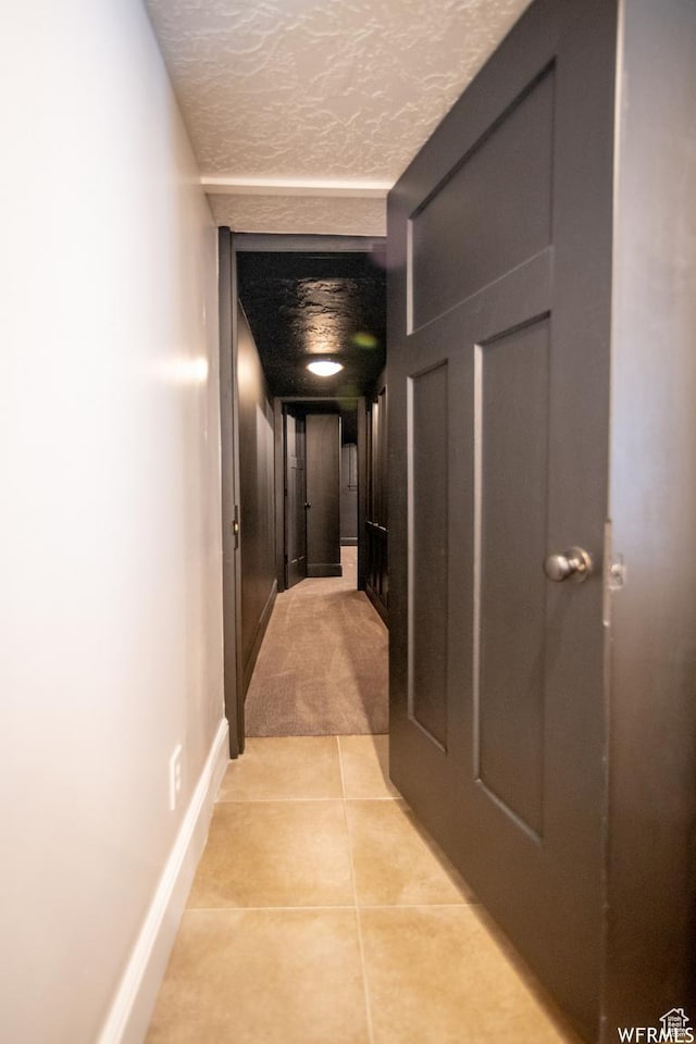 hall featuring light tile patterned floors, baseboards, and a textured ceiling