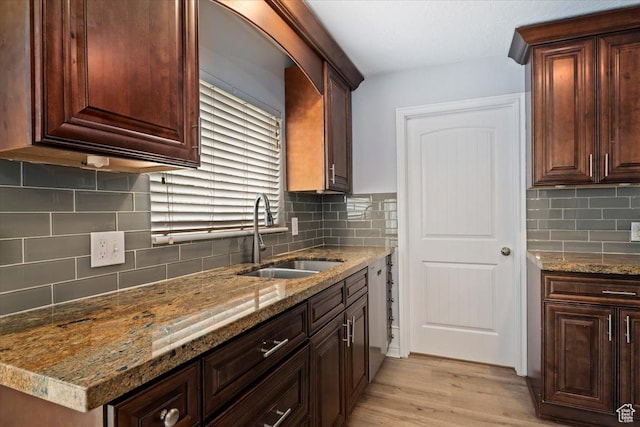 kitchen featuring a sink, backsplash, light wood finished floors, light stone counters, and dishwasher