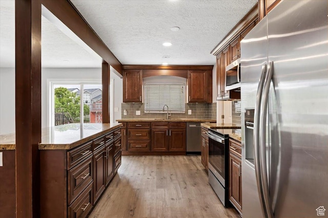 kitchen featuring appliances with stainless steel finishes, a sink, light wood-style flooring, a textured ceiling, and decorative backsplash