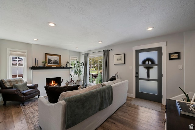 living area featuring a tiled fireplace, wood finished floors, a textured ceiling, recessed lighting, and baseboards