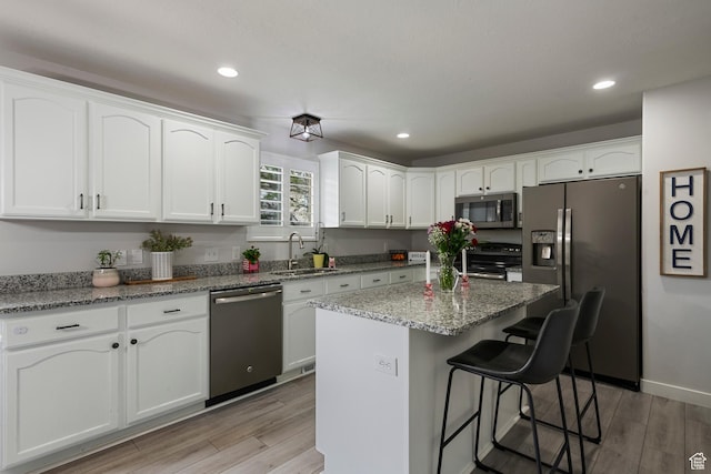 kitchen with stainless steel appliances, a sink, white cabinets, a kitchen breakfast bar, and recessed lighting