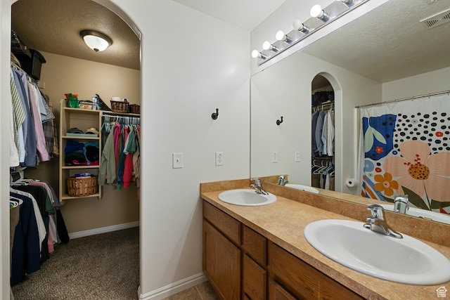 full bath featuring a walk in closet, double vanity, baseboards, and a textured ceiling