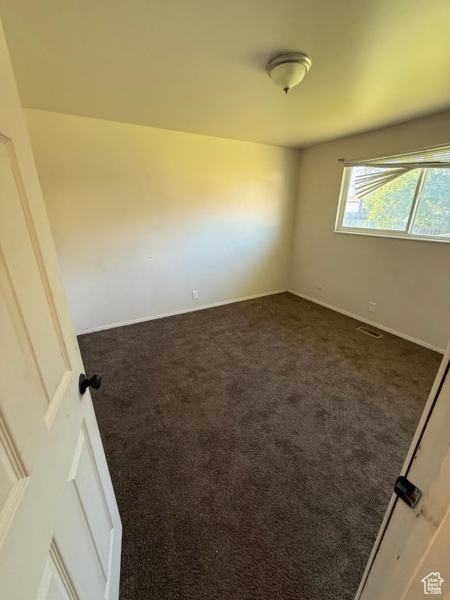 empty room featuring dark carpet and baseboards