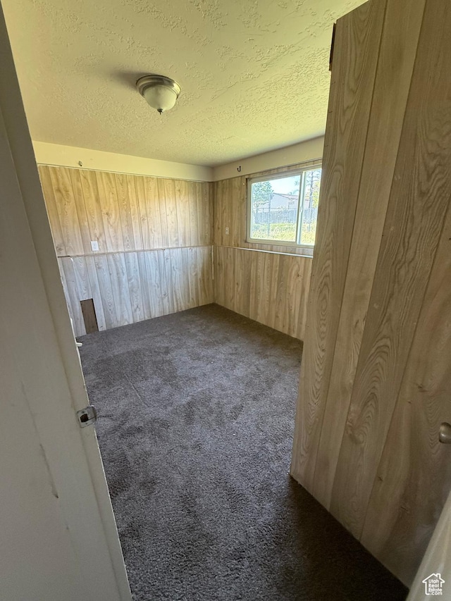 carpeted empty room with wooden walls and a textured ceiling