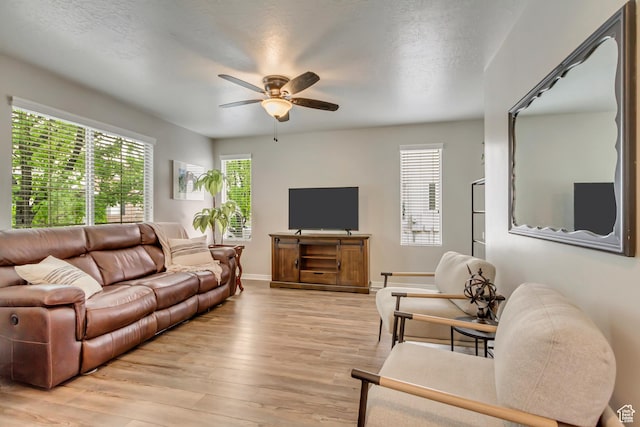 living area with a ceiling fan, healthy amount of natural light, light wood-style floors, and baseboards