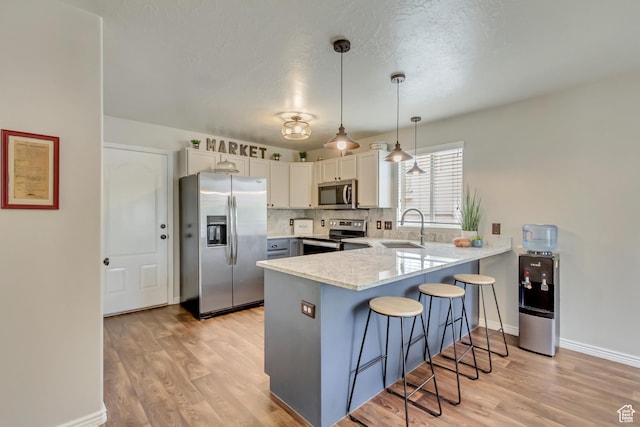 kitchen with stainless steel appliances, a peninsula, a kitchen breakfast bar, and light wood finished floors