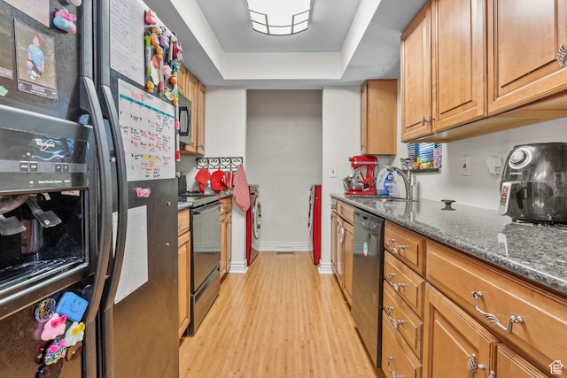 kitchen featuring black appliances, washer / dryer, light wood-type flooring, a sink, and brown cabinetry