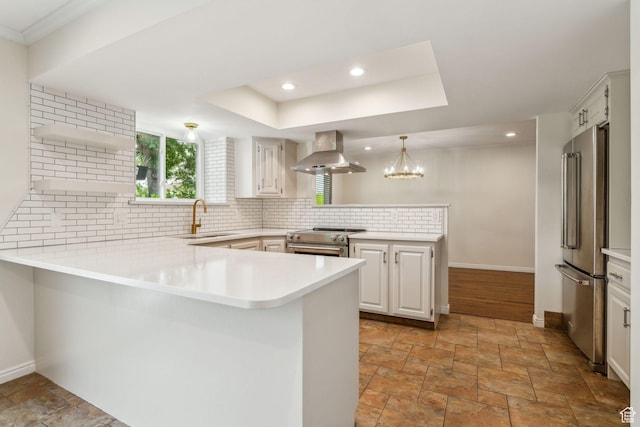 kitchen with wall chimney range hood, a peninsula, a sink, high end appliances, and stone tile flooring