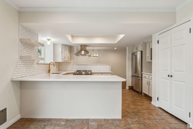 kitchen with stainless steel appliances, a peninsula, wall chimney range hood, light countertops, and stone finish floors