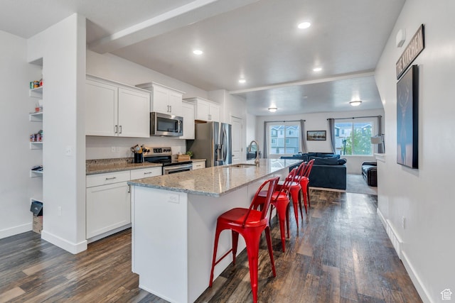 kitchen featuring appliances with stainless steel finishes, a sink, dark wood finished floors, open floor plan, and white cabinets