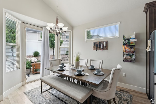dining area with a chandelier, light wood-type flooring, vaulted ceiling, and baseboards