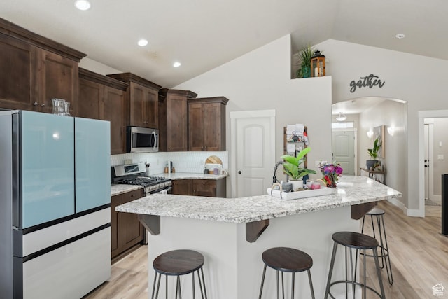 kitchen featuring stainless steel appliances, a breakfast bar, arched walkways, light wood finished floors, and dark brown cabinets