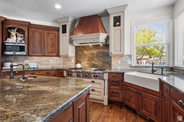kitchen with custom exhaust hood, stainless steel microwave, a sink, glass insert cabinets, and recessed lighting