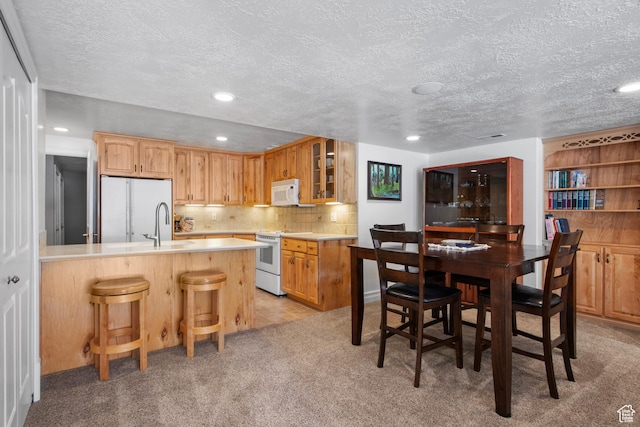 kitchen featuring white appliances, light countertops, glass insert cabinets, a breakfast bar area, and a peninsula