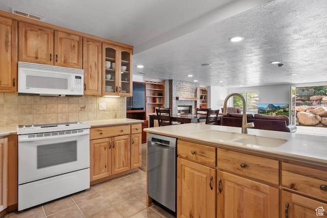 kitchen featuring white appliances, a sink, a large fireplace, light countertops, and tasteful backsplash