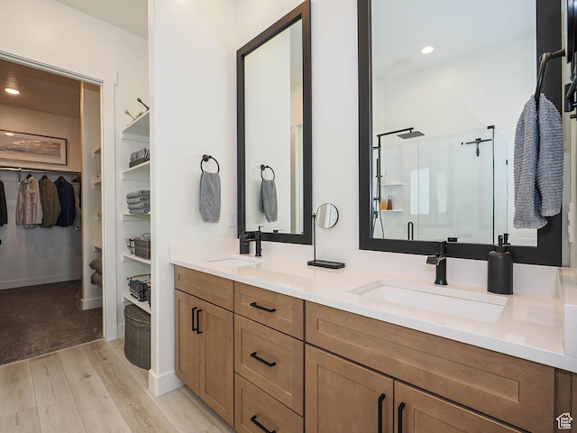 full bath with wood finished floors, a shower stall, a spacious closet, double vanity, and recessed lighting