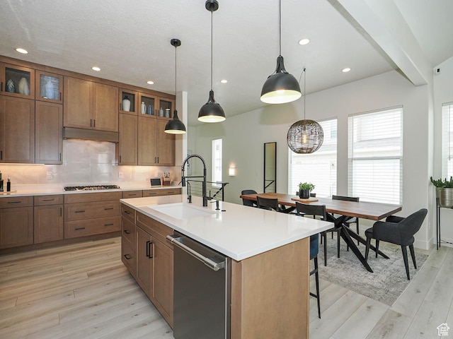 kitchen with a sink, stainless steel appliances, brown cabinets, light countertops, and recessed lighting