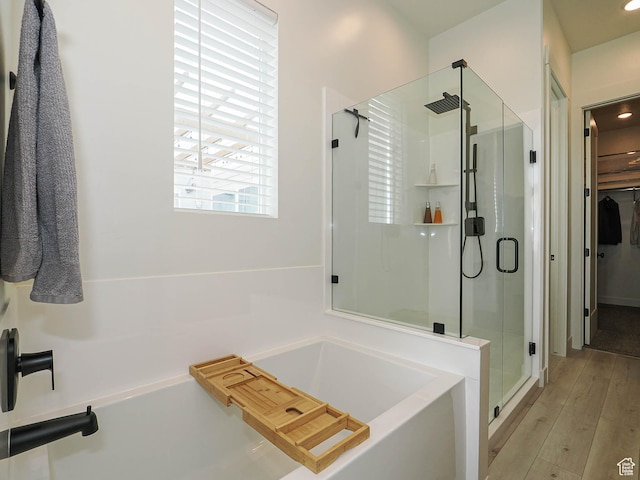 full bathroom with a stall shower, a garden tub, wood finished floors, and a walk in closet