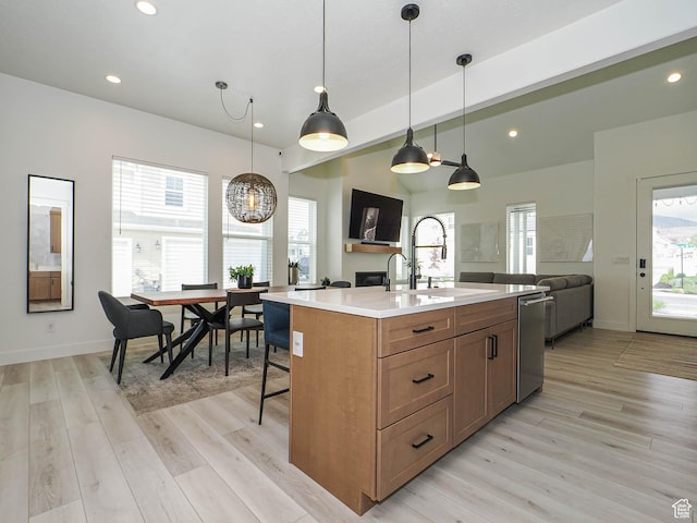 kitchen featuring dishwasher, a sink, light countertops, open floor plan, and light wood-style floors