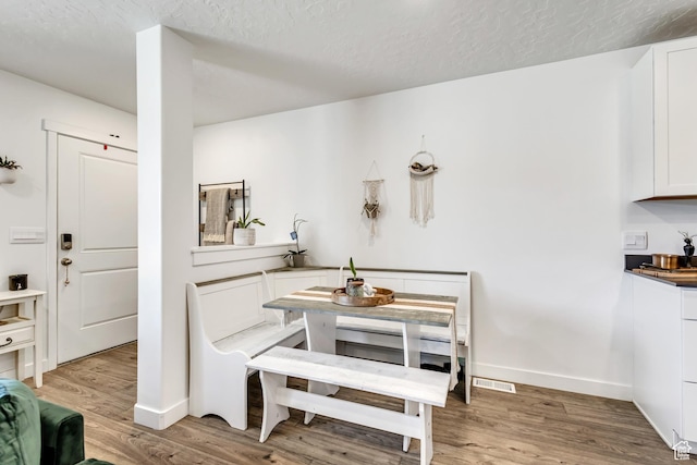 dining room featuring light wood-style floors, a textured ceiling, and baseboards
