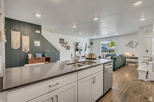 kitchen featuring dishwasher, a sink, white cabinetry, dark countertops, and wood finished floors