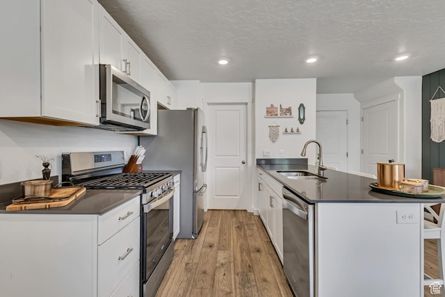 kitchen featuring stainless steel appliances, a sink, dark countertops, a peninsula, and light wood-type flooring