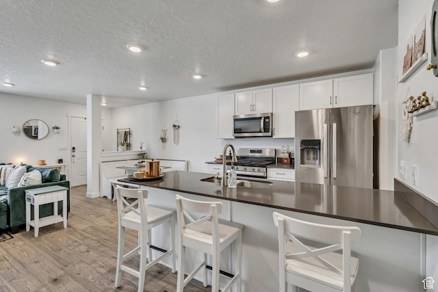 kitchen with stainless steel appliances, dark countertops, a sink, light wood finished floors, and a breakfast bar area