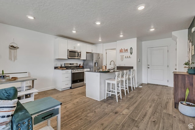 kitchen featuring stainless steel appliances, dark countertops, a kitchen breakfast bar, light wood-style floors, and white cabinetry