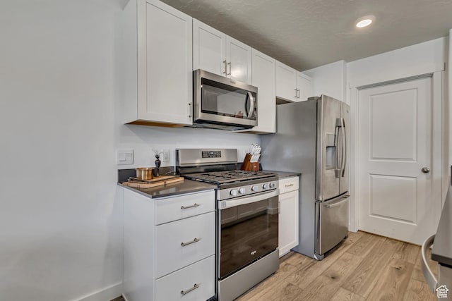 kitchen with stainless steel appliances, light wood-type flooring, dark countertops, white cabinets, and recessed lighting