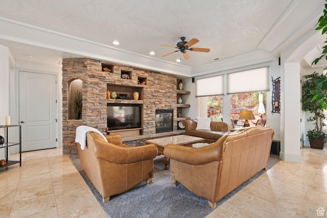 living area featuring a ceiling fan, a stone fireplace, a raised ceiling, recessed lighting, and baseboards
