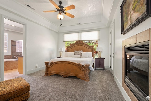 bedroom featuring light carpet, a raised ceiling, connected bathroom, baseboards, and a ceiling fan