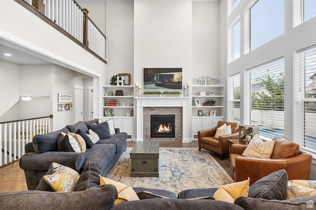living area with a towering ceiling, wood finished floors, a warm lit fireplace, and built in features