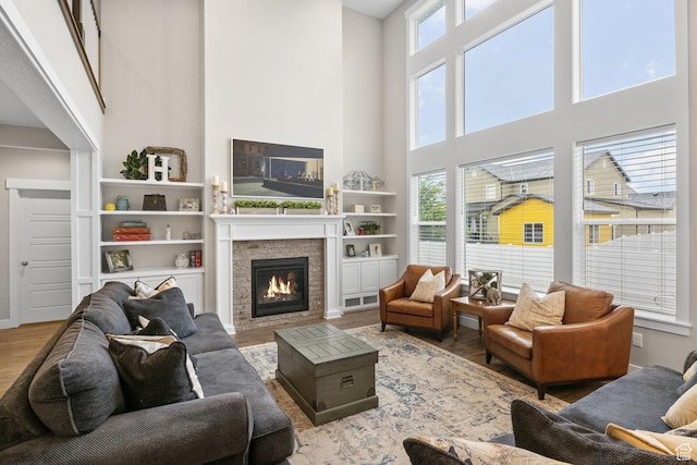 living area featuring a high ceiling, wood finished floors, plenty of natural light, and a glass covered fireplace