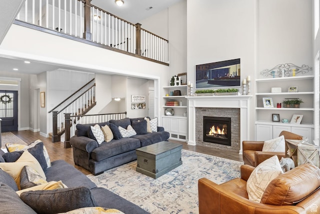 living area featuring a high ceiling, wood finished floors, built in features, a stone fireplace, and stairs
