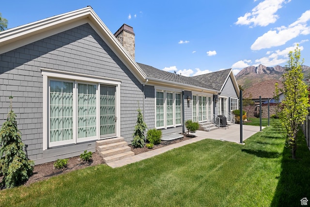 back of property with entry steps, a patio area, a chimney, a mountain view, and roof with shingles