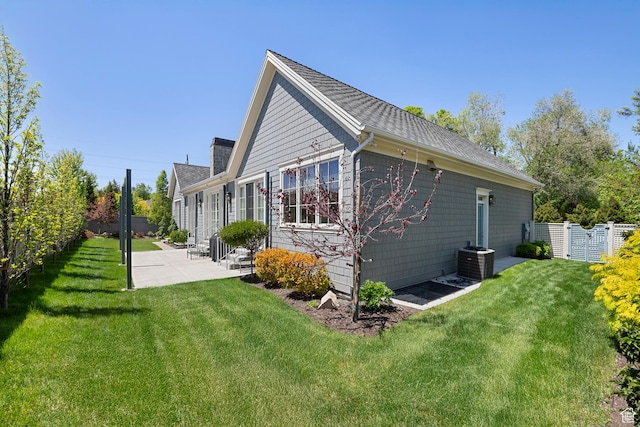 view of side of home with central AC, a patio, a chimney, and roof with shingles
