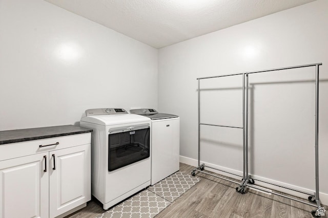 laundry room featuring washing machine and clothes dryer, light wood-style floors, cabinet space, baseboards, and a textured ceiling