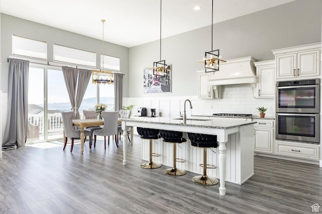 kitchen with a sink, stainless steel appliances, a towering ceiling, light stone countertops, and a breakfast bar area