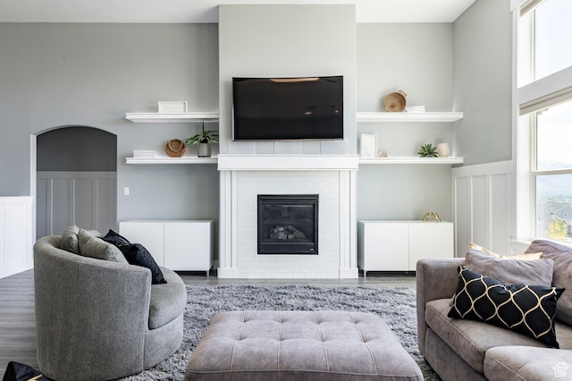 living room featuring wood finished floors, a decorative wall, wainscoting, and a fireplace