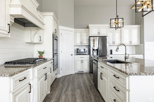 kitchen featuring appliances with stainless steel finishes, a sink, a chandelier, backsplash, and custom exhaust hood