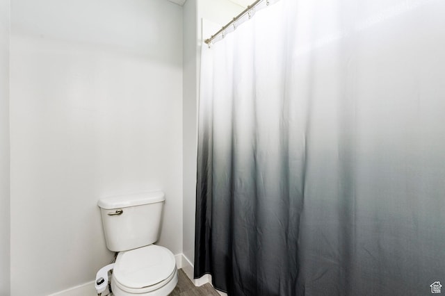 bathroom featuring baseboards, toilet, and curtained shower