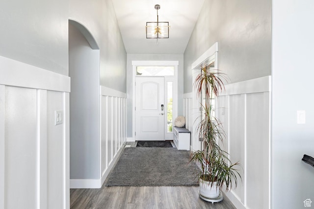 foyer entrance featuring wood finished floors, arched walkways, a wainscoted wall, and a decorative wall