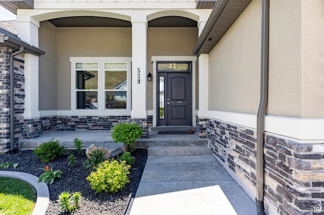 property entrance with covered porch, stucco siding, and stone siding